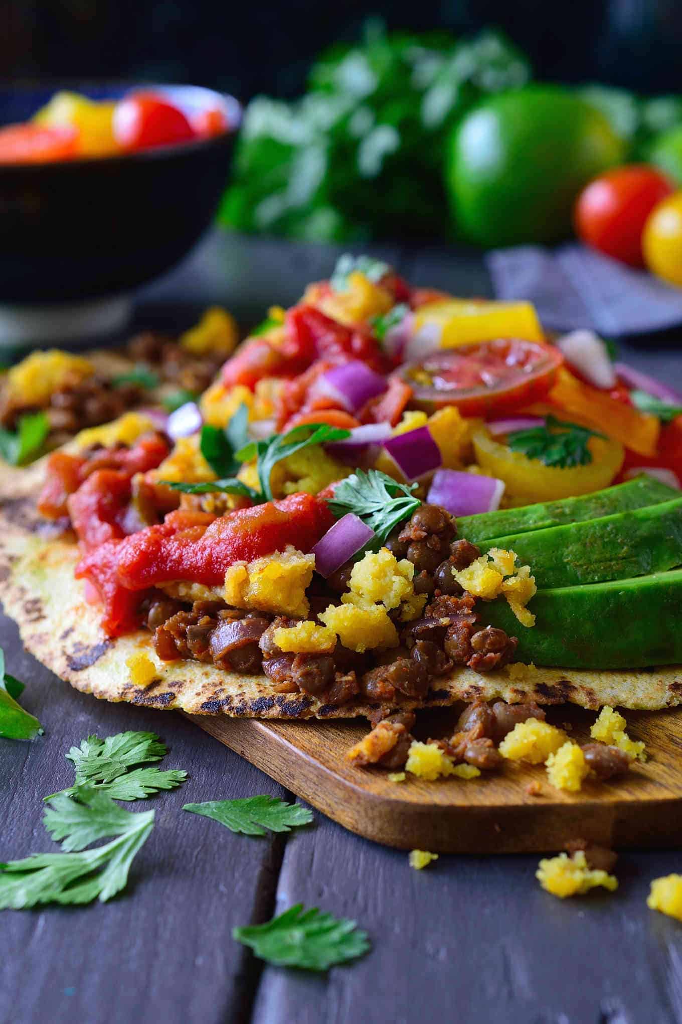 nyitott taco egy táblán, amelyen lencse, csicseriborsó lisztes tojás, paradicsom és avokádó töltése látható.