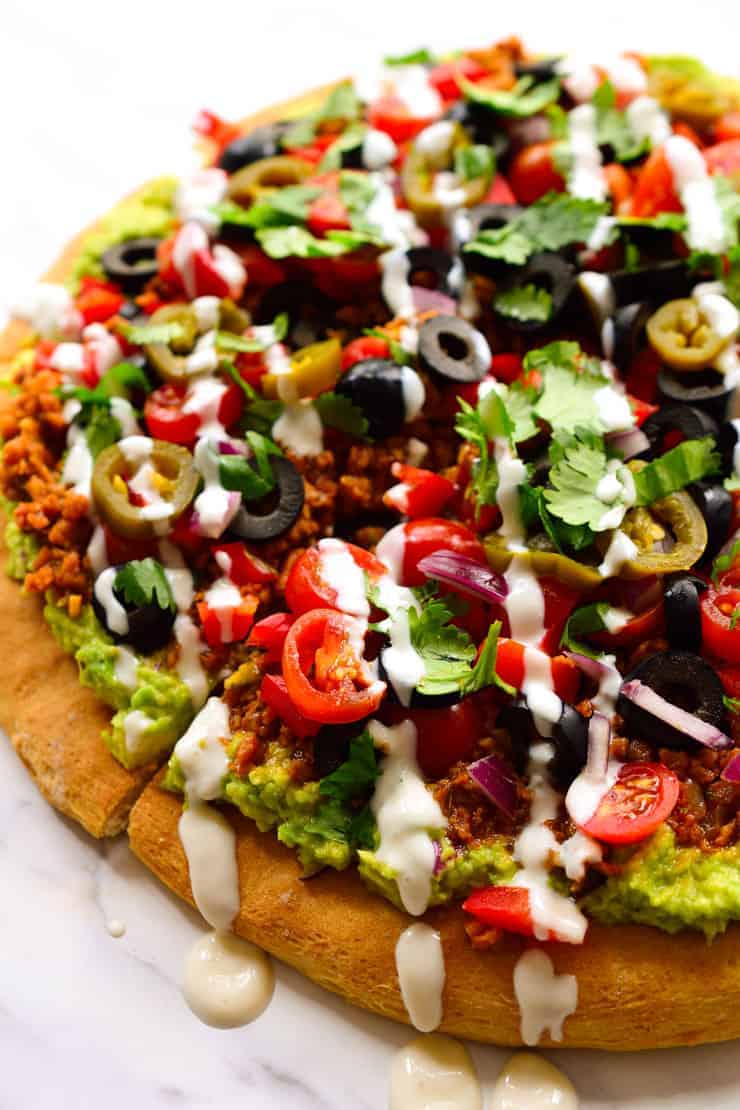 Vegan nacho pizza is a pizza with nacho toppings. Am I blowing your mind right now? A pizza crust slathered with guacamole and topped with vegan taco meat, veggies, jalapeños, cilantro and vegan sour cream. How many days can I live off this?
