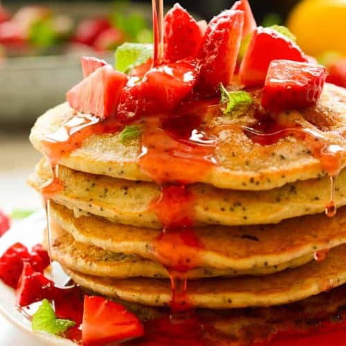 A stack of vegan strawberry pancakes with syrup being poured over.