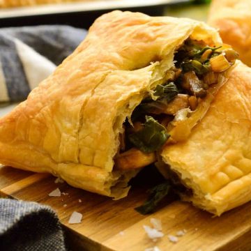A puff pastry pocked pulled open on a cutting board exposing the chard and mushroom filling.