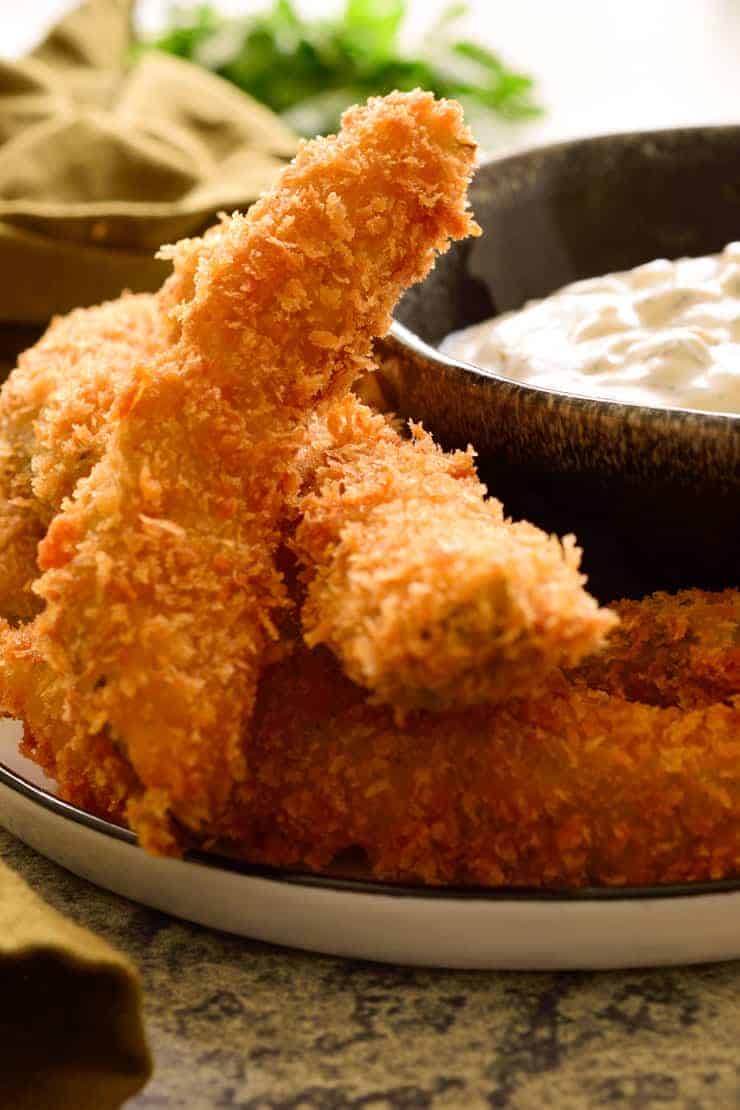 A pile of fried pickles on a plate with a black bowl of ranch dip.