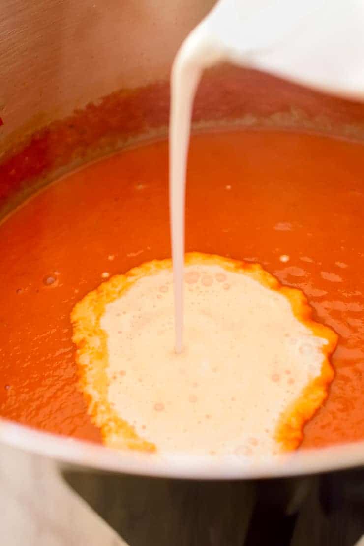 Pouring coconut milk into the pot of tomato soup.