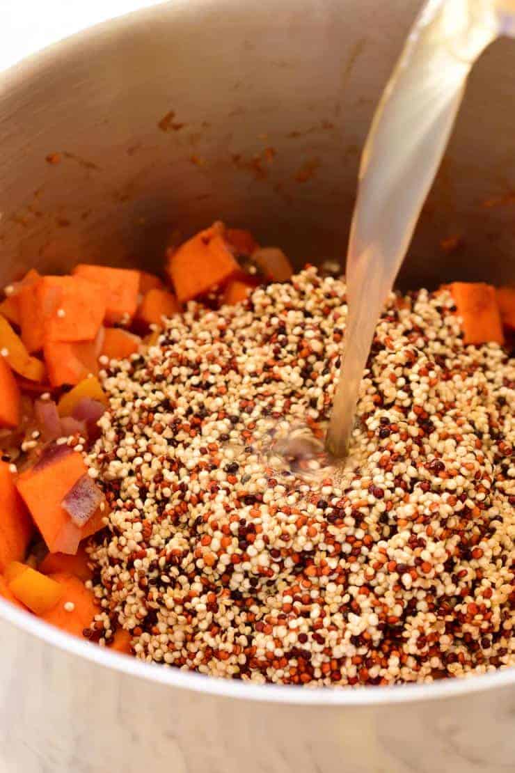 A pot of sweet potatoes and three coloured quinoa. Pouring the vegetable stock into the pot.
