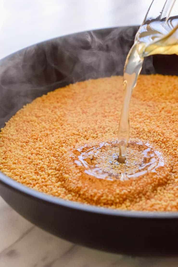 Pouring vegetable stock into a pan of toasted couscous.