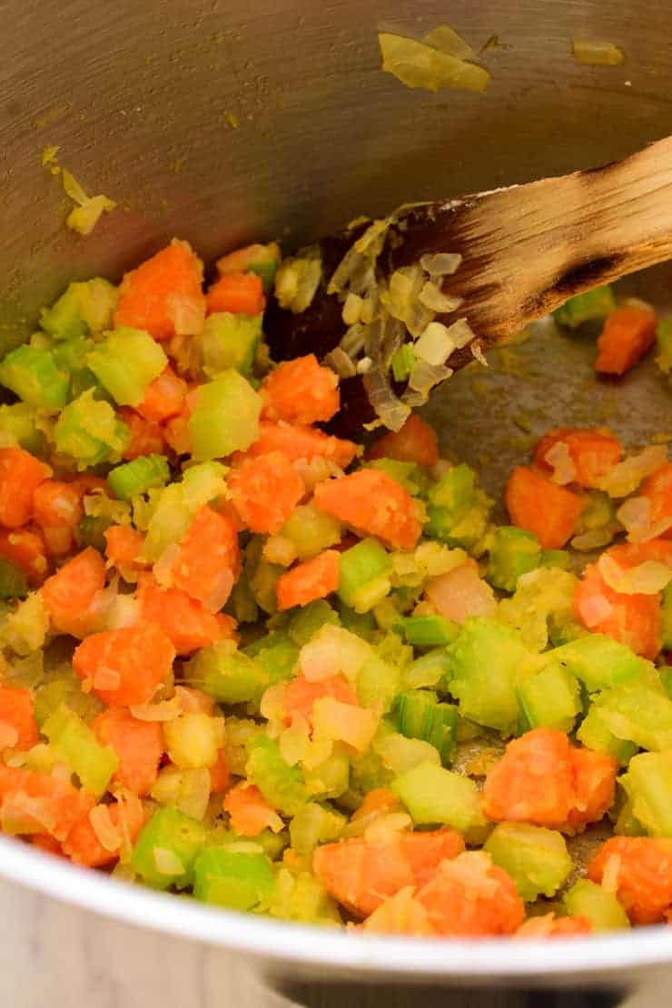 Onion, celery, carrots and flour frying in a pot with a wooden spoon.