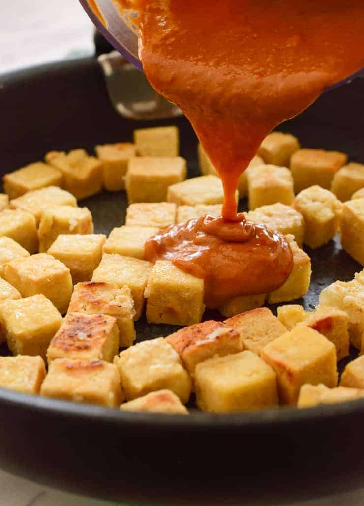 Pouring the sauce over the crispy tofu in a black pan.