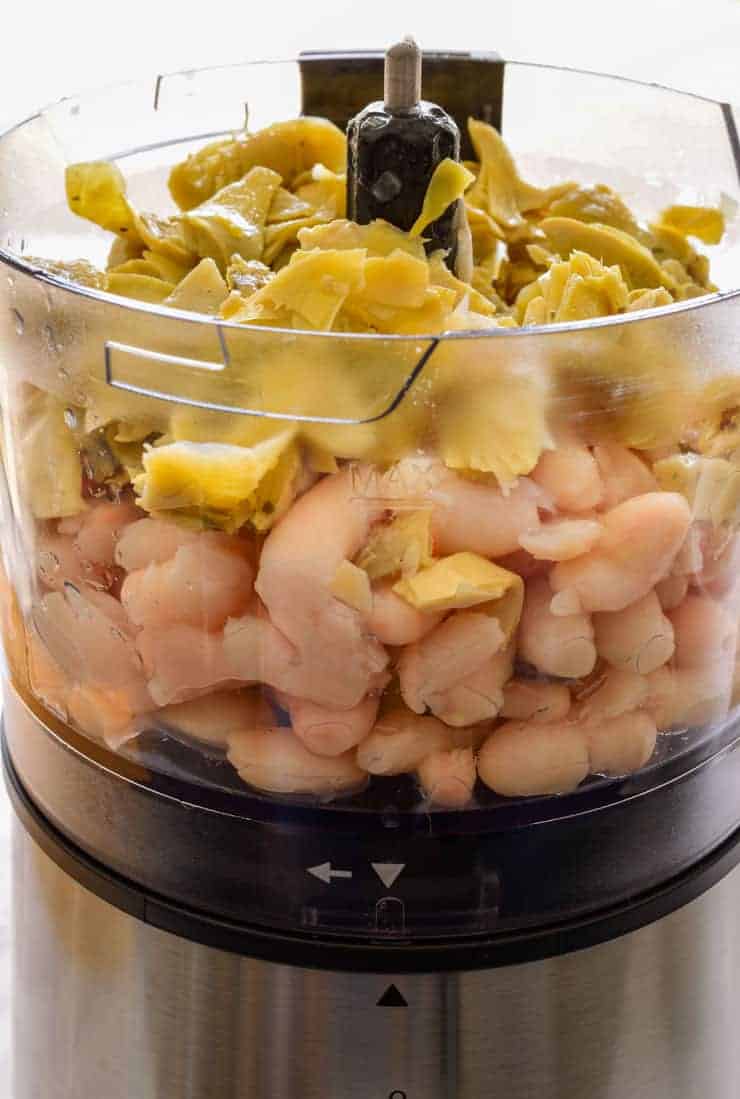Beans and artichoke hearts in the bowl of a food processor before blending.