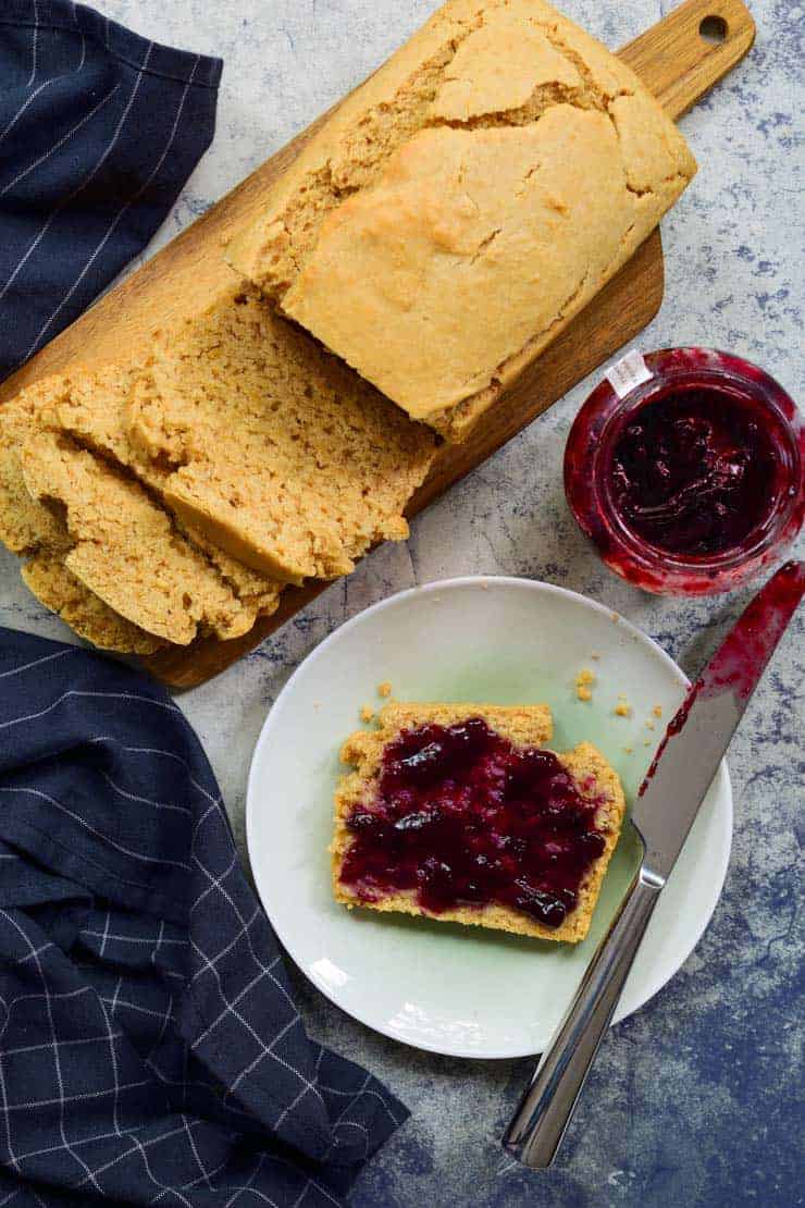 An overhead shot of the loaf of peanut butter bread and a slice with jam on it on a plate.