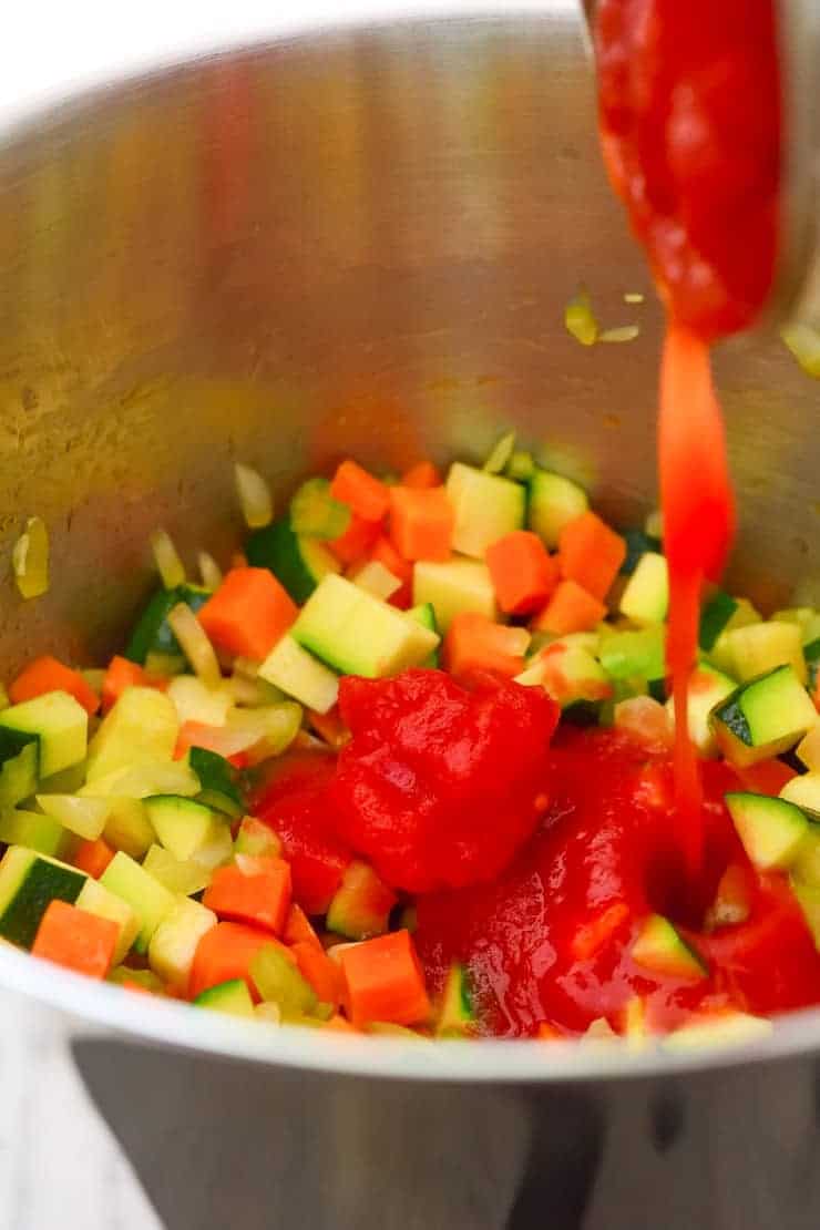 Pouring the tomatoes into the pot with the vegetables.