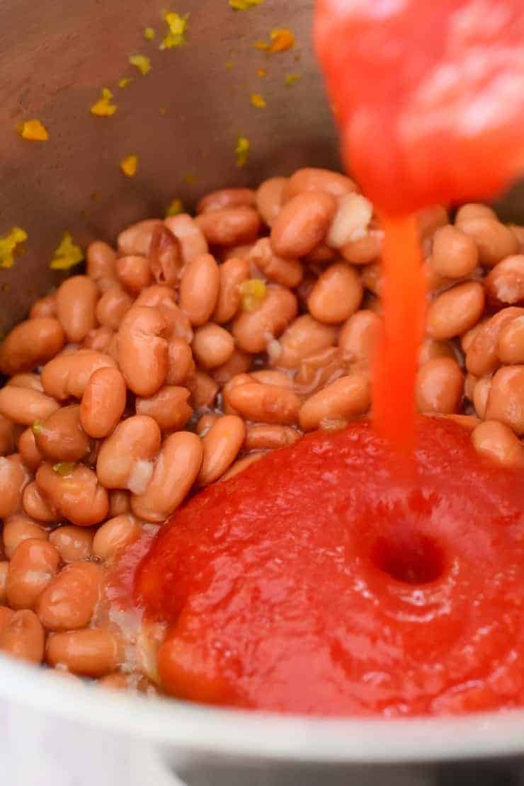 Pouring crushed tomatoes into the pot with the beans.