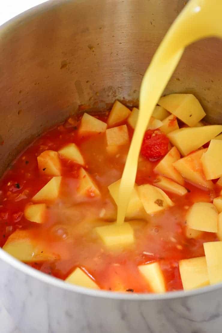 Pouring vegetable stock into the pot with the potatoes and tomatoes.