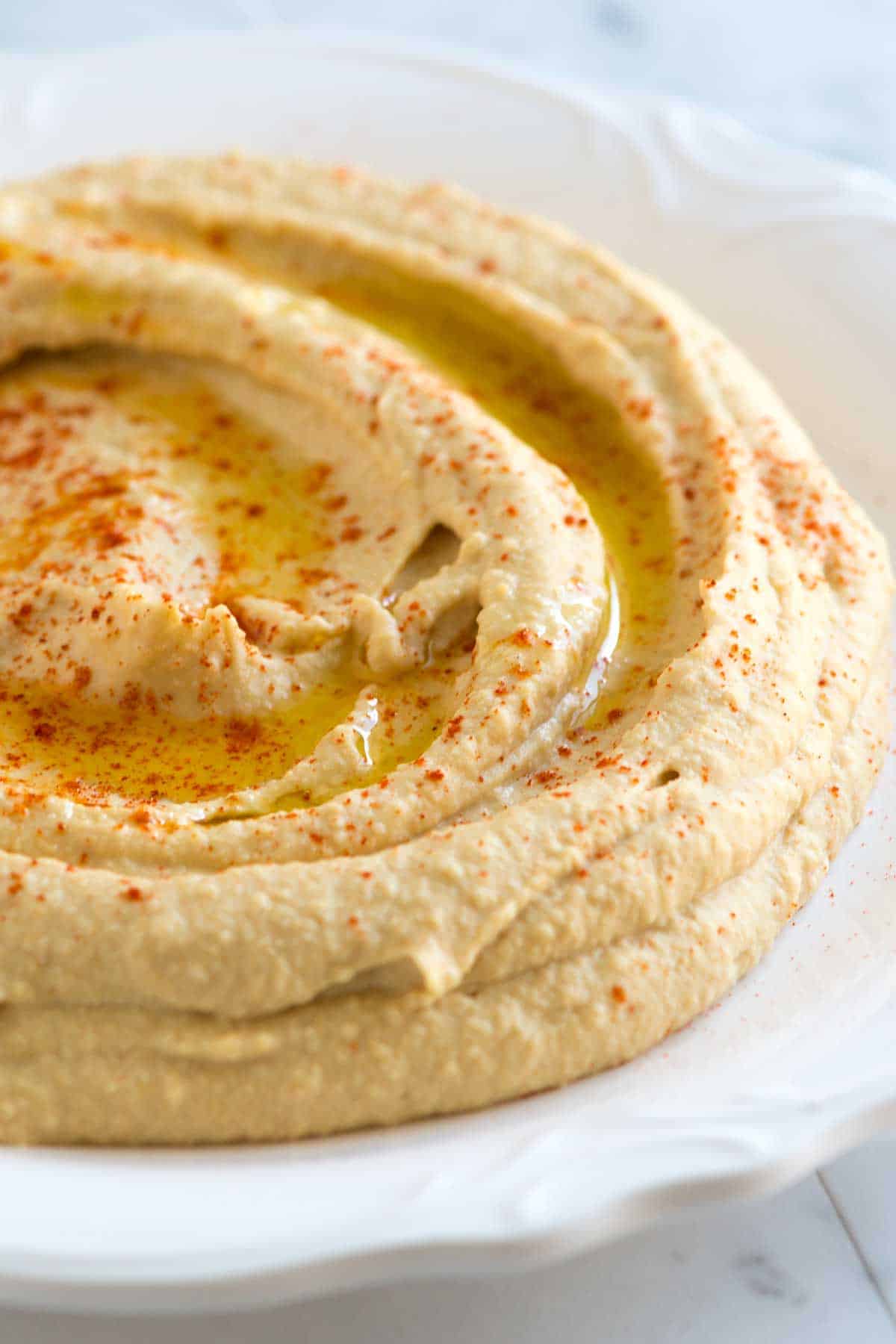 A close-up shot of hummus on a white plate and garnished with olive oil and paprika.