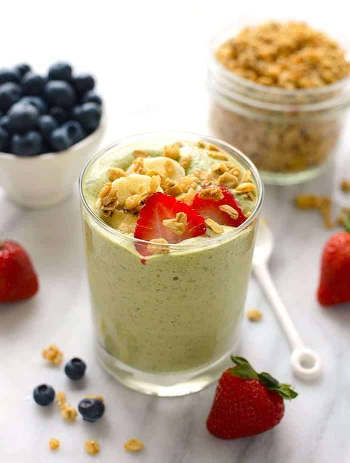 A cup filled with green smoothie and decorated with granola and strawberries.