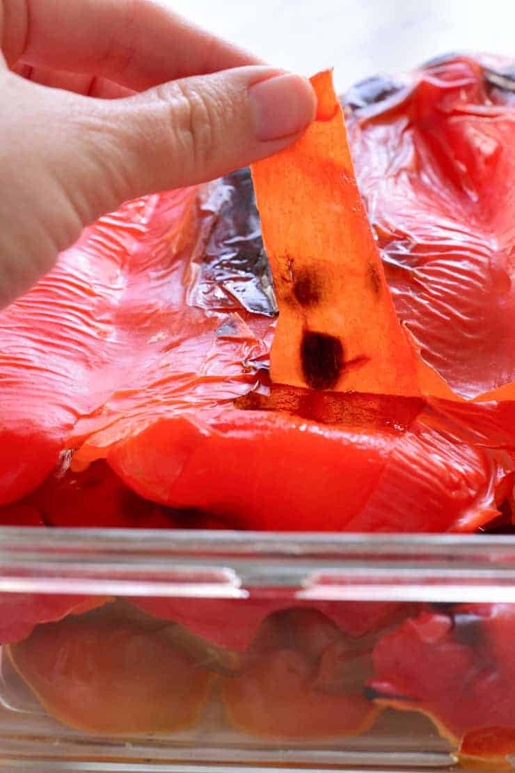 A hand peeling the charred skin off of a roasted red pepper.
