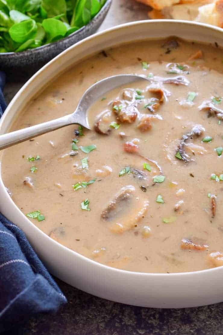 A white bowl of vegan cream of mushroom soup with a spoon in it.