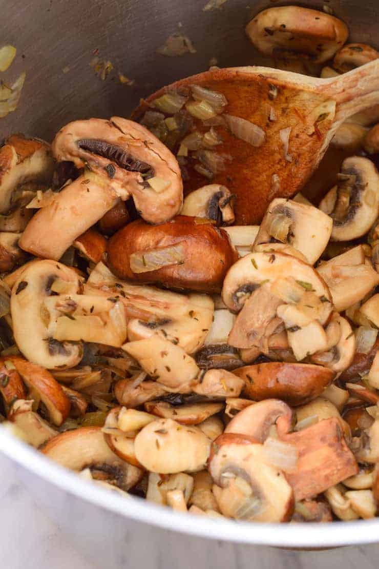 The sautéed mushrooms for vegan cream of mushroom soup in the pot with a wooden spoon.