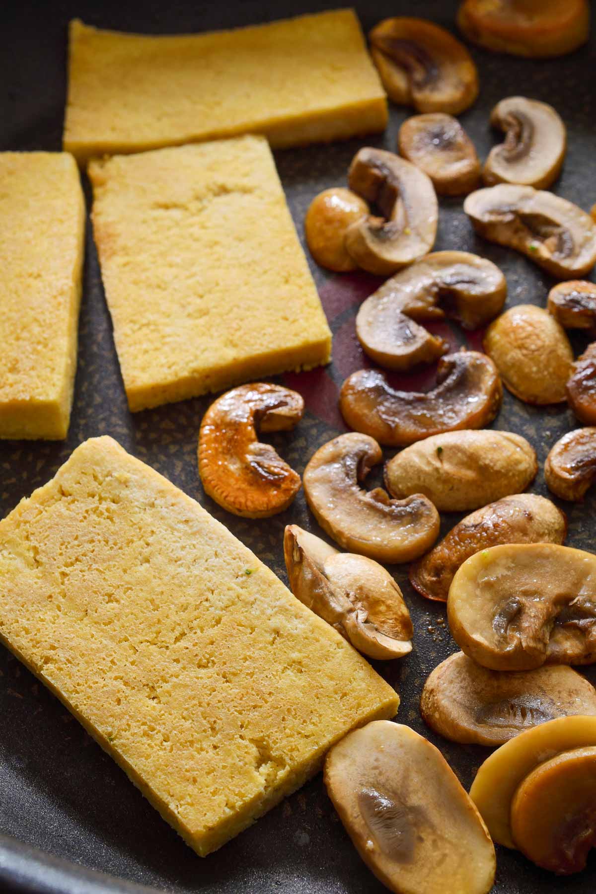 A pan with fried tofu slices and mushrooms.