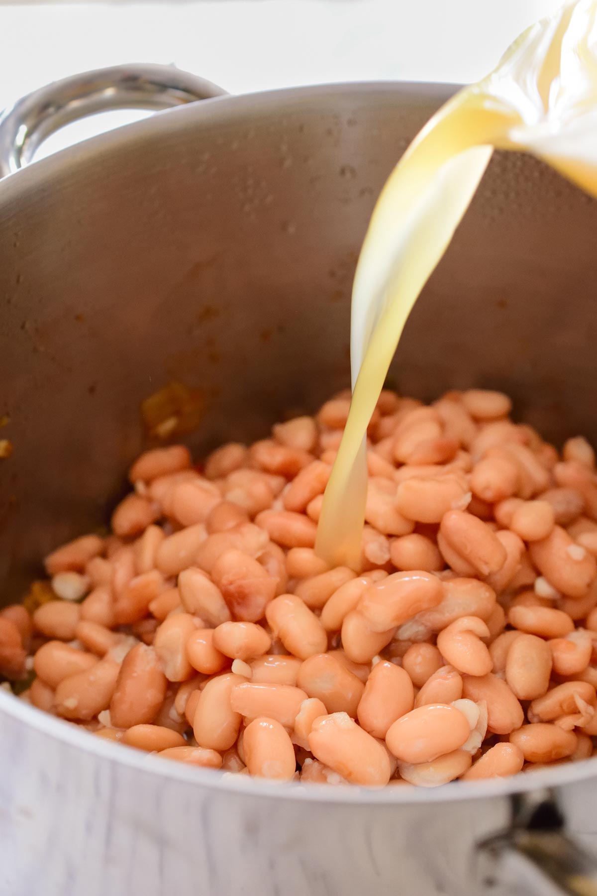 Pouring vegetable stock into the pot full of pinto beans.