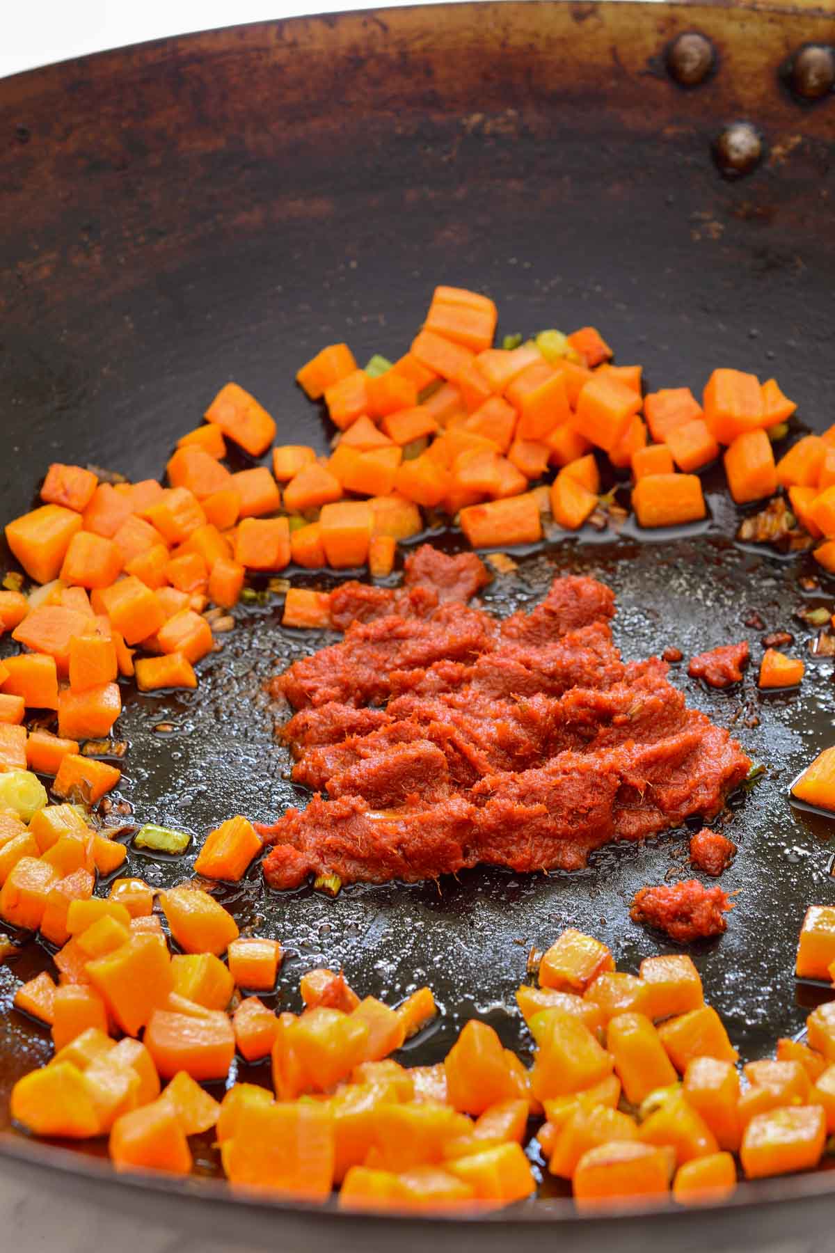 A wok with carrots pushed to the side and curry paste in the middle.