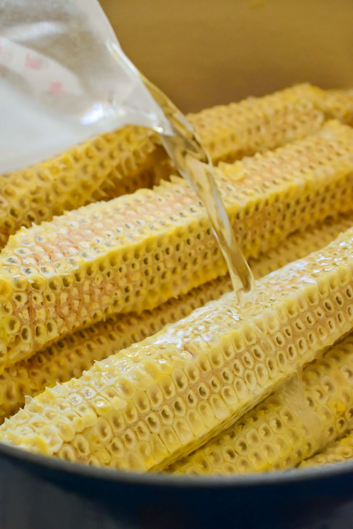 Naked corn cobs in a pot with water being poured over.