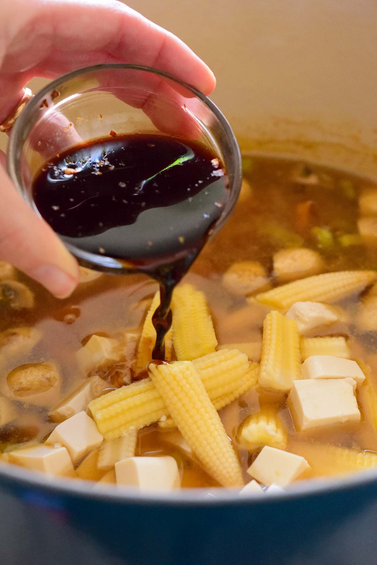 Pouring soy sauce from a small glass bowl into the soup pot.