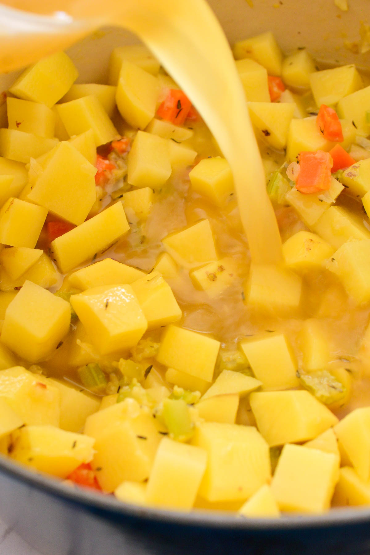 Pouring vegetable stock into the pot of potatoes and veggies,