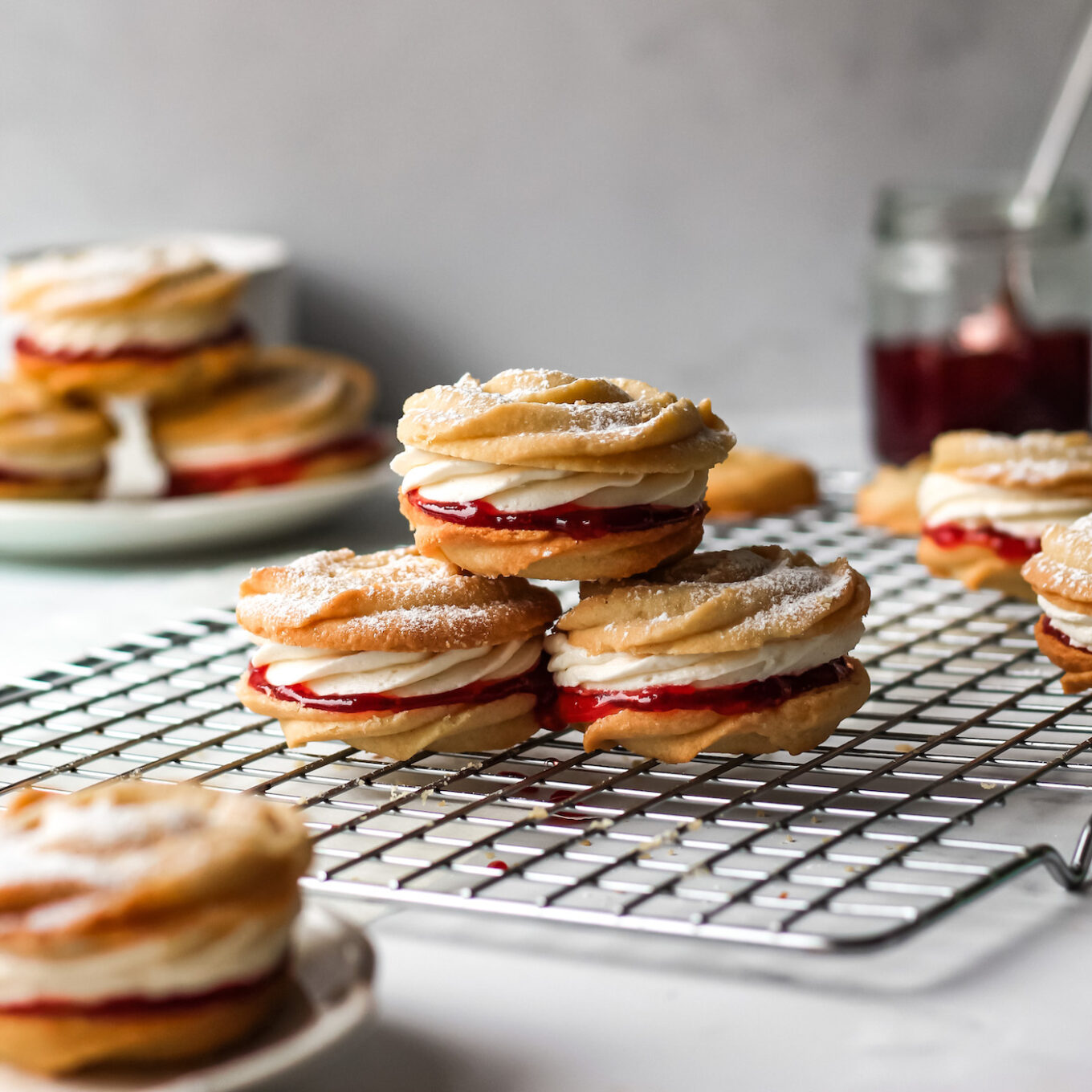Jam and cream-filled round cookies on a cooling rack.