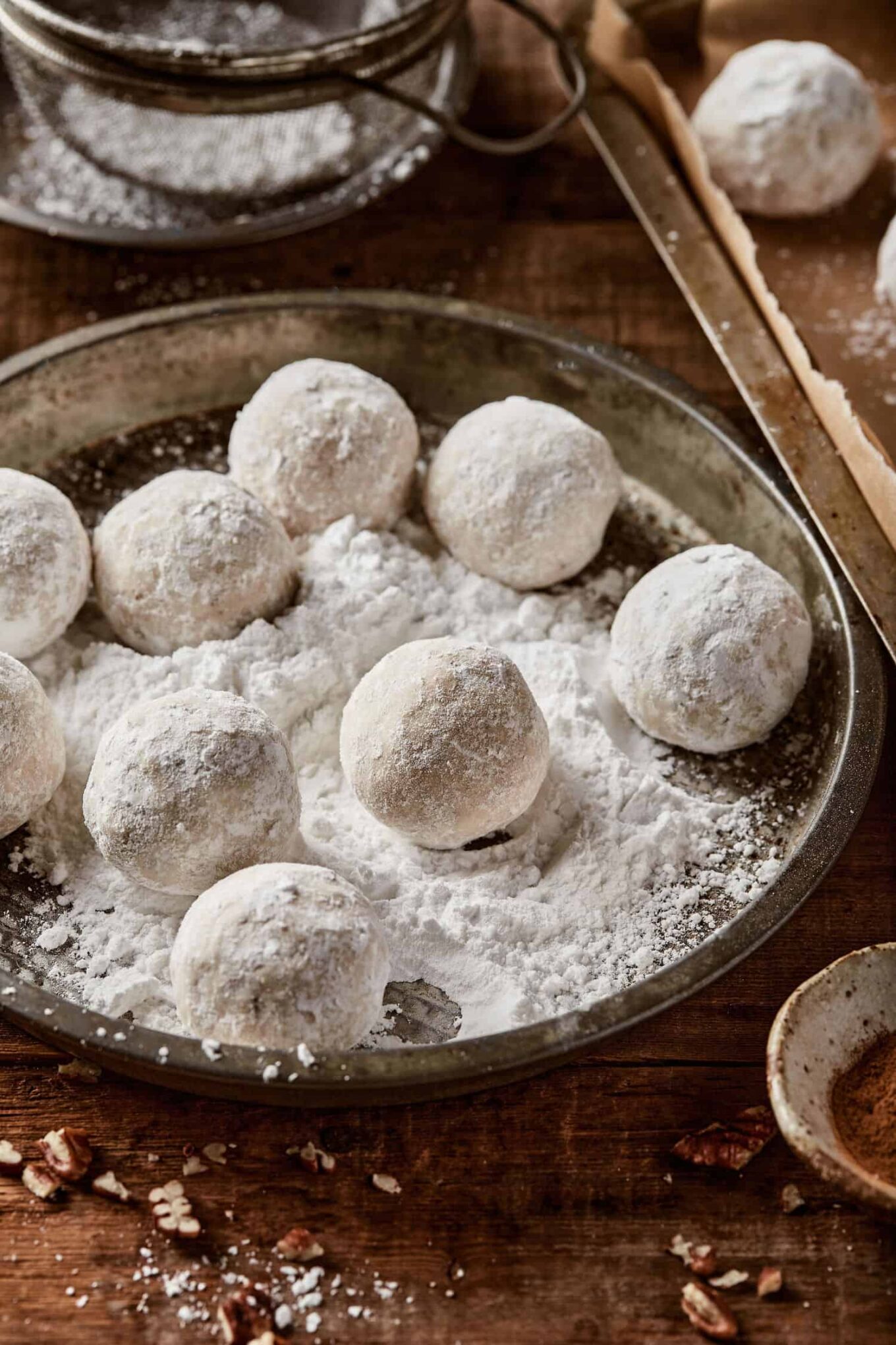 A metal pan with snowball cookies sitting on a bed of icing sugar.