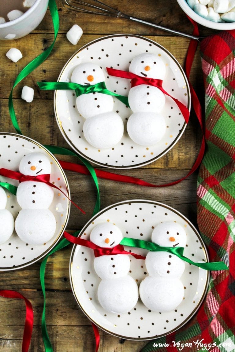 Three plates with two meringue snowmen with red and green bows around their necks.