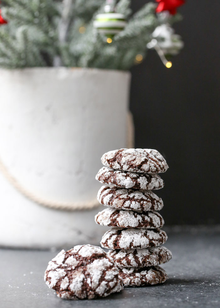 A stack of chocolate crinkle cookies and a Christmas tree branch in the background.