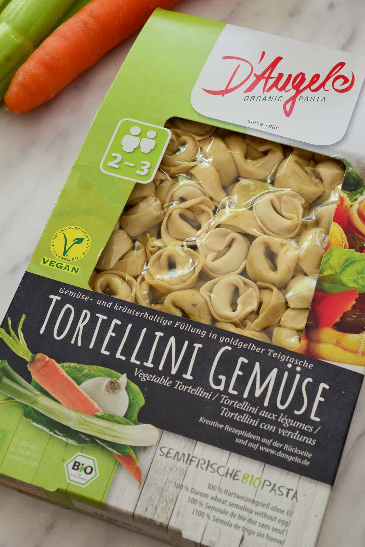A package of vegan tortellini on the counter with a carrot and celery beside it.