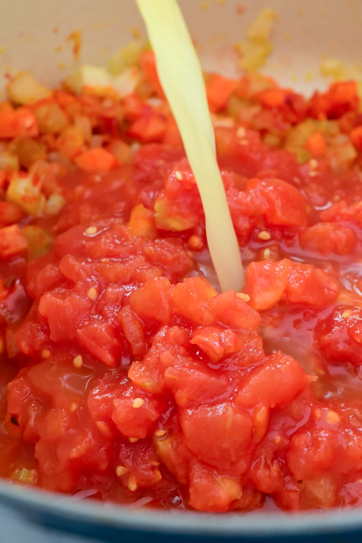 Pouring vegetable stock over diced tomatoes in the pot of tortellini soup.