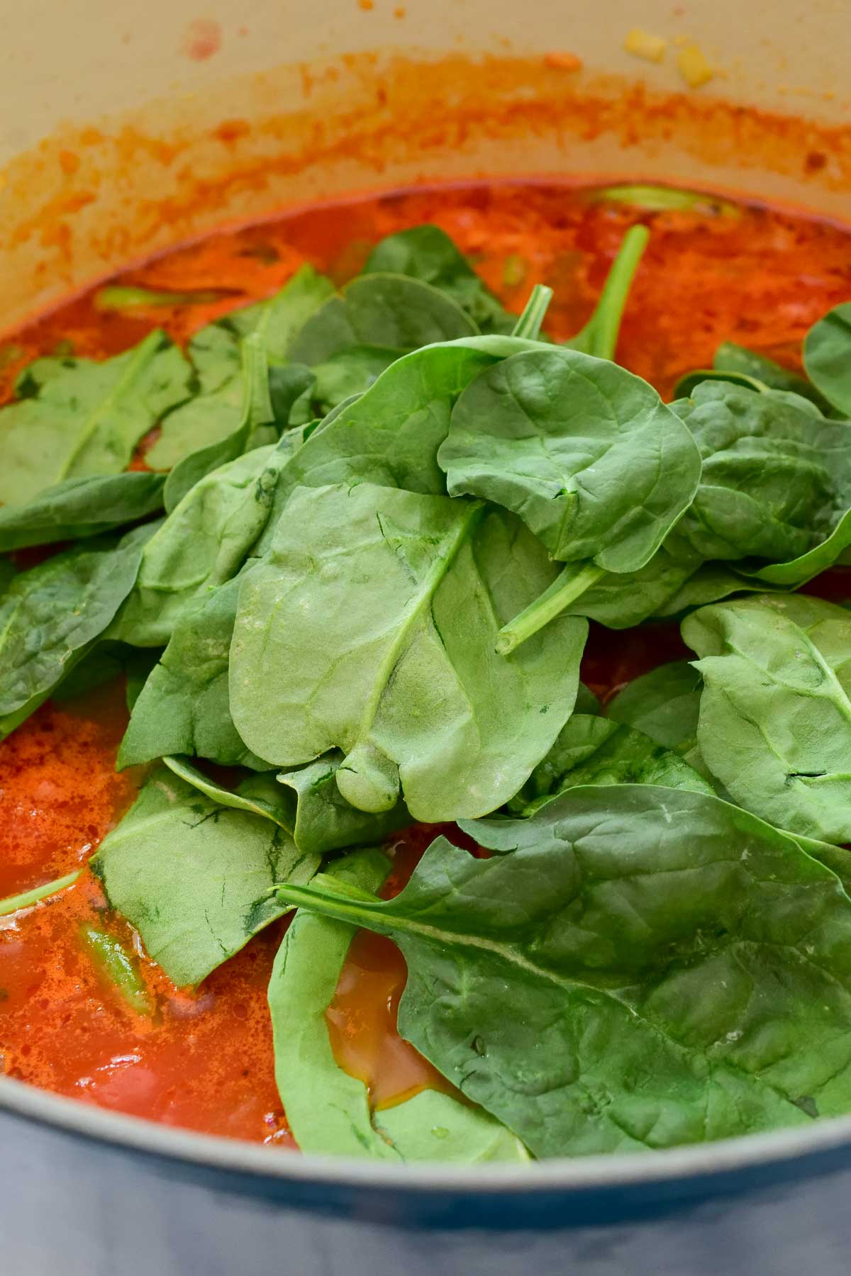 A pile of spinach on top of the pot of soup.