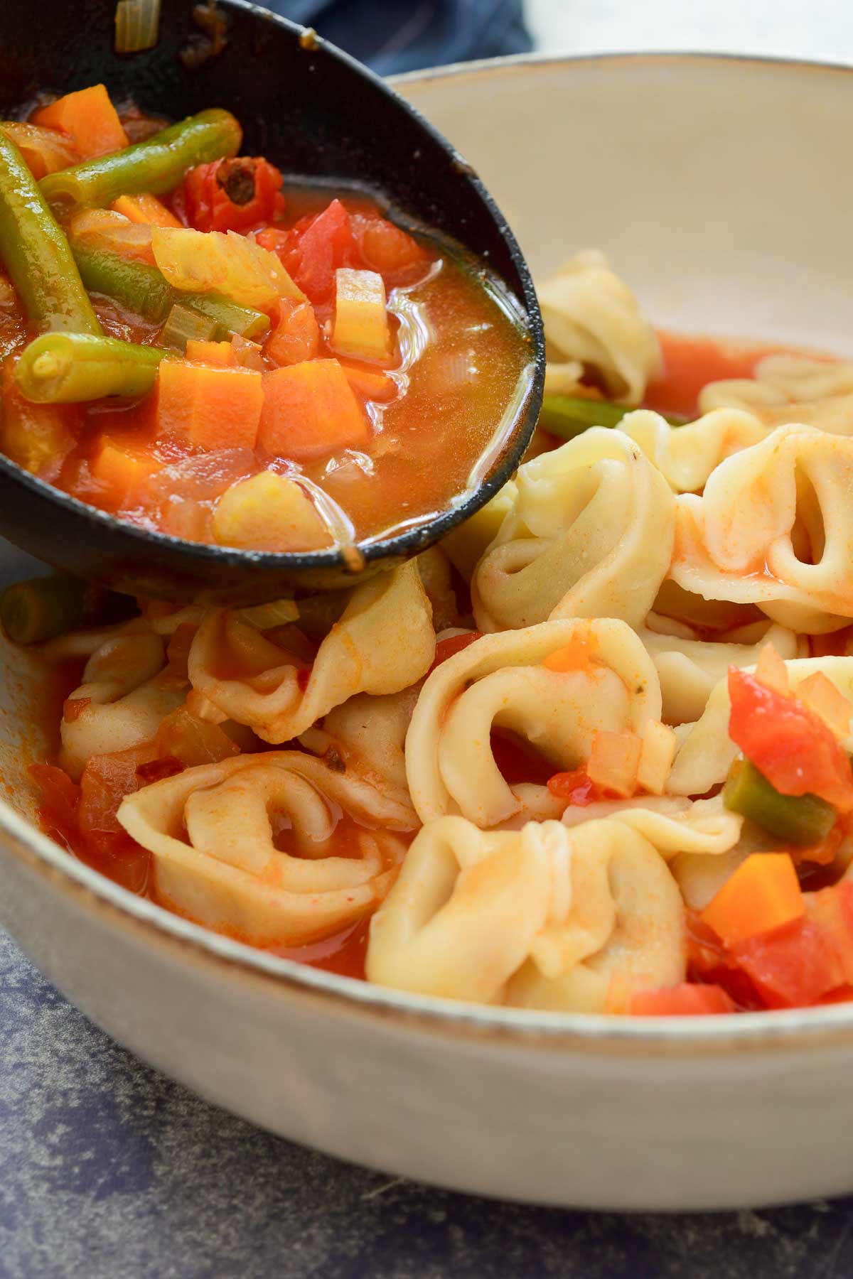 Pouring vegetable soup over cooked tortellini in a bowl.