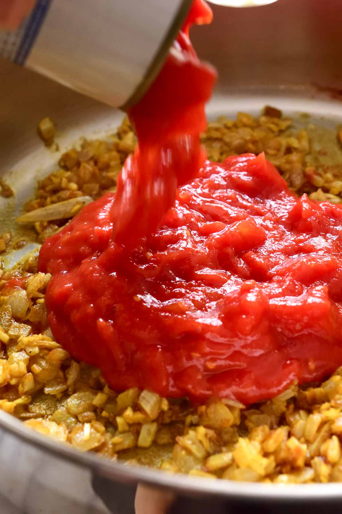 pouring a can of diced tomatoes into the pan.