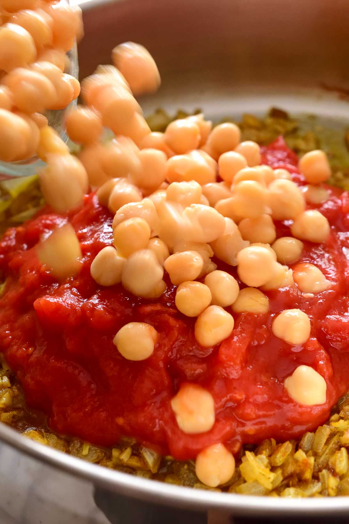 Pouring the chickpeas into the pan over the diced tomatoes.