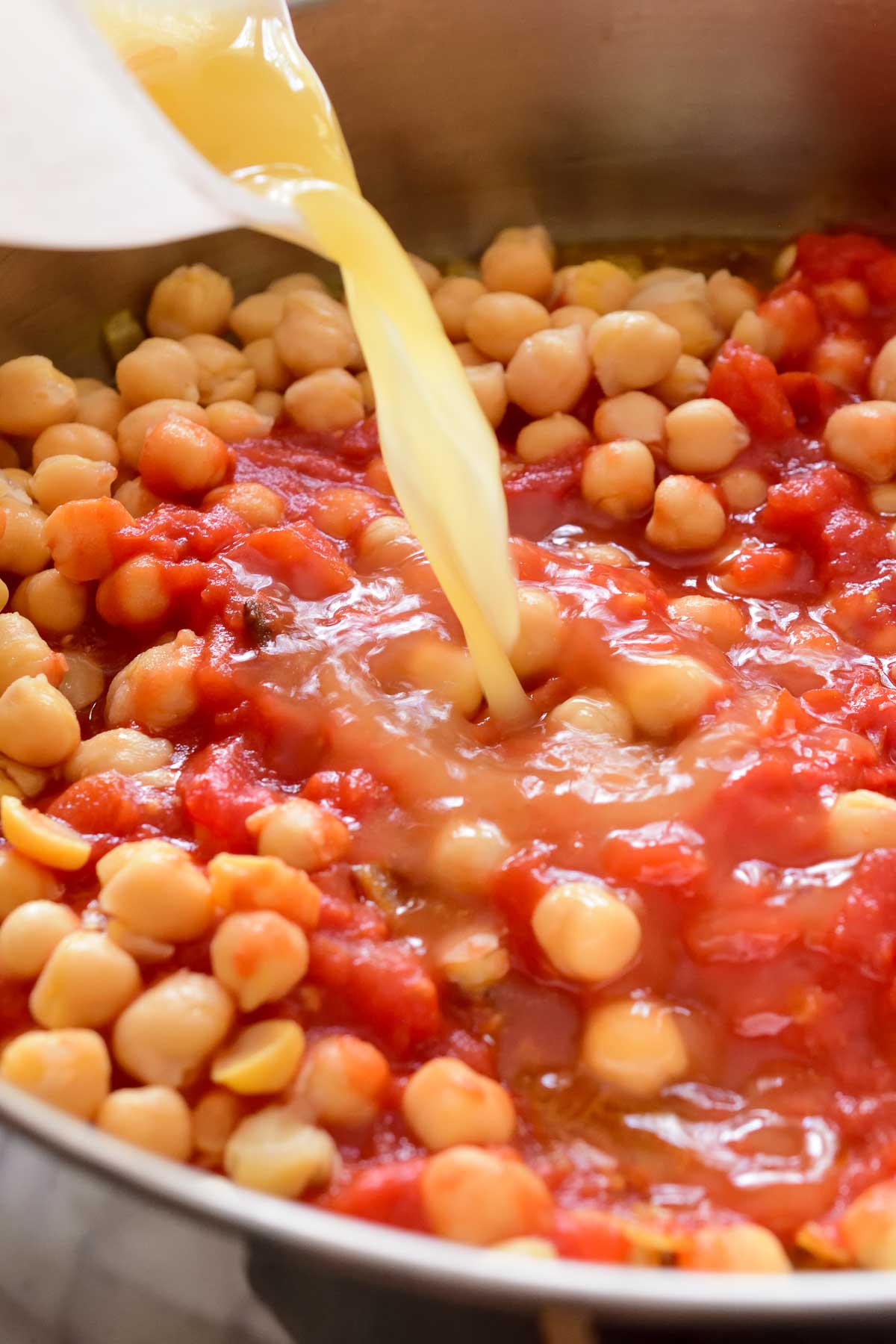 Pouring vegetable stock into the pan with tomatoes and chickpeas.