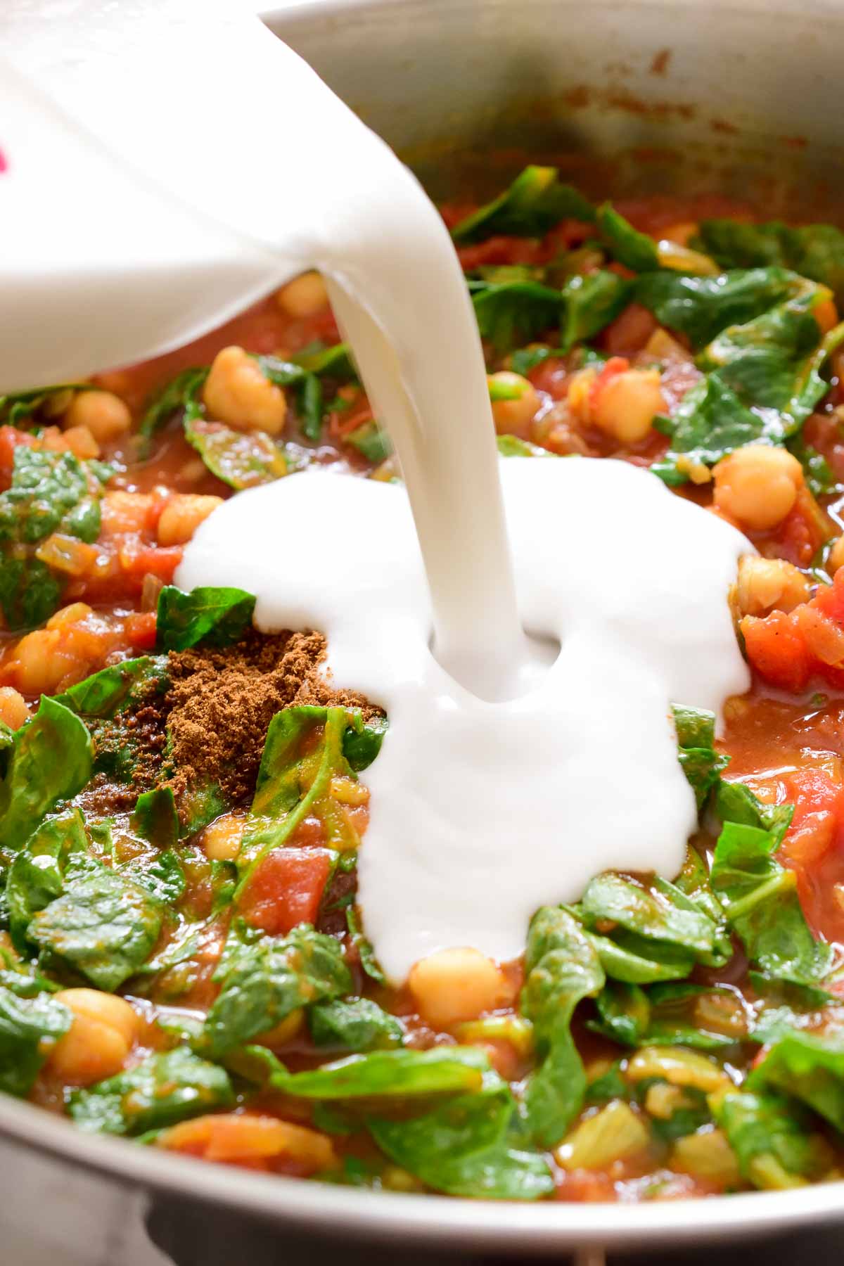 Pouring coconut milk into the pan of coconut chickpea curry.