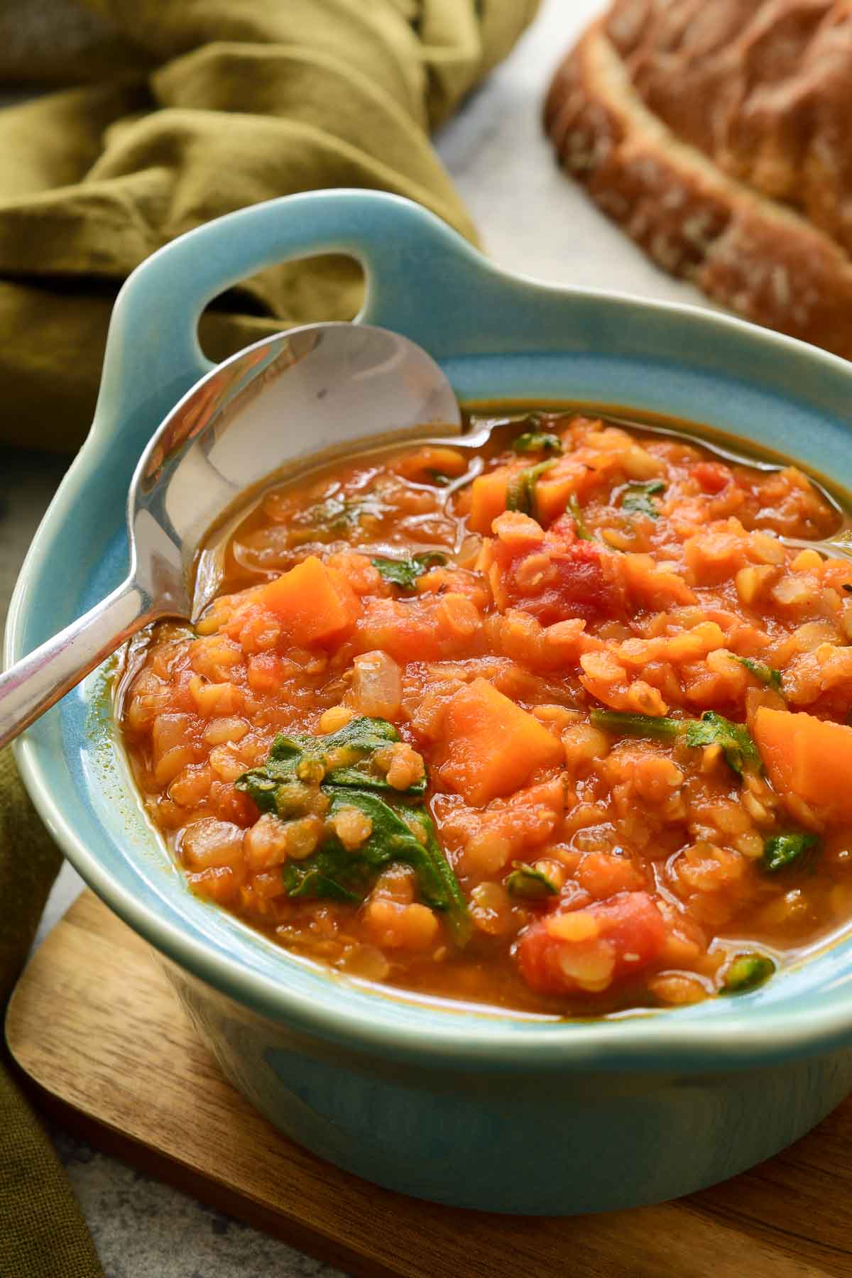 A blue dish of red lentil stew with a spoon in it.