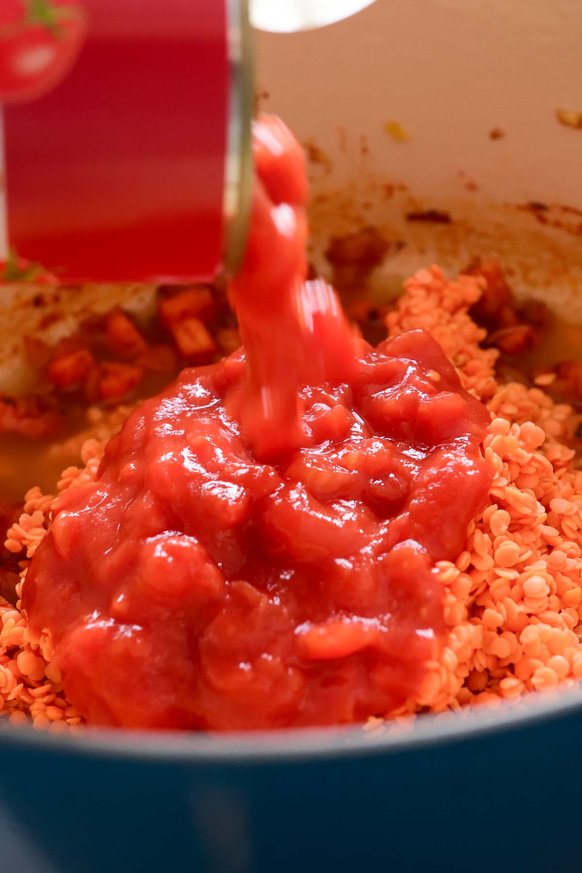 Pouring diced tomatoes over red lentils in a pot.