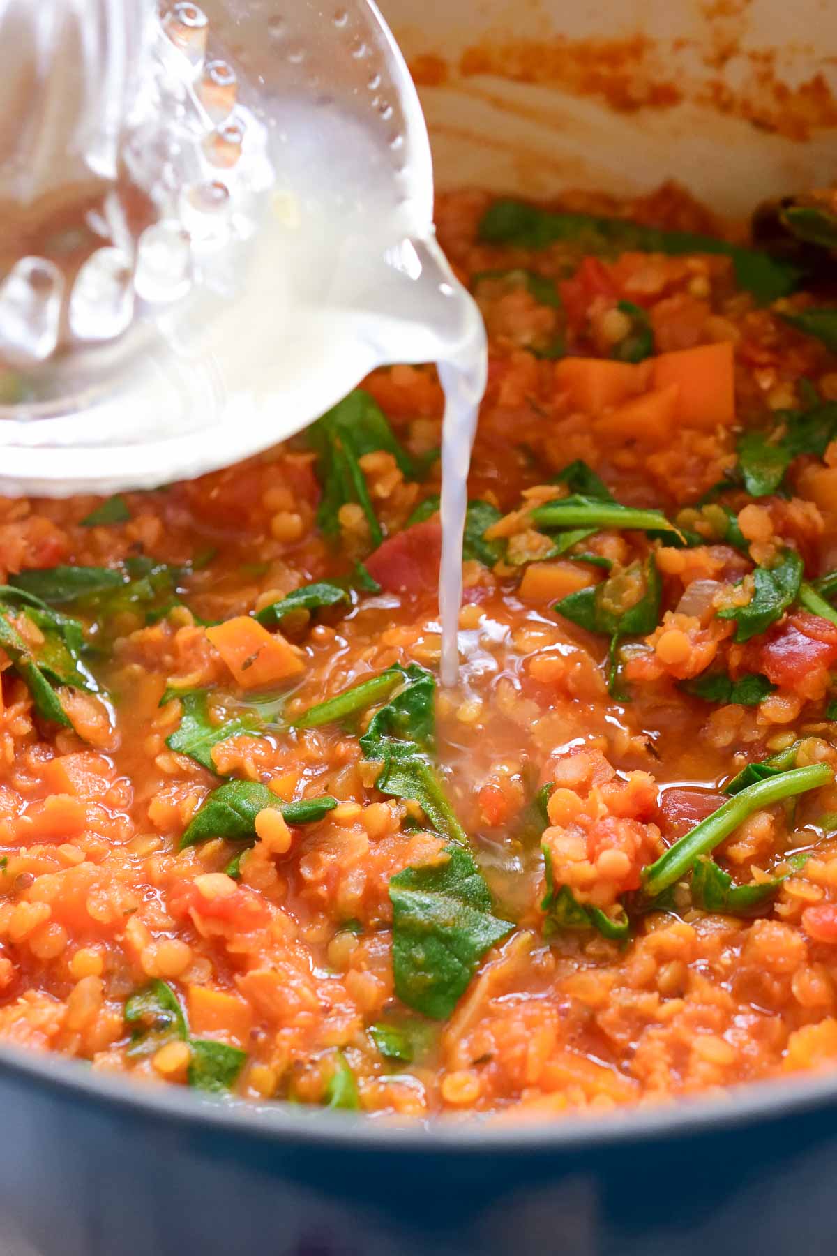 Pouring lemon juice into a pot of red lentil stew.