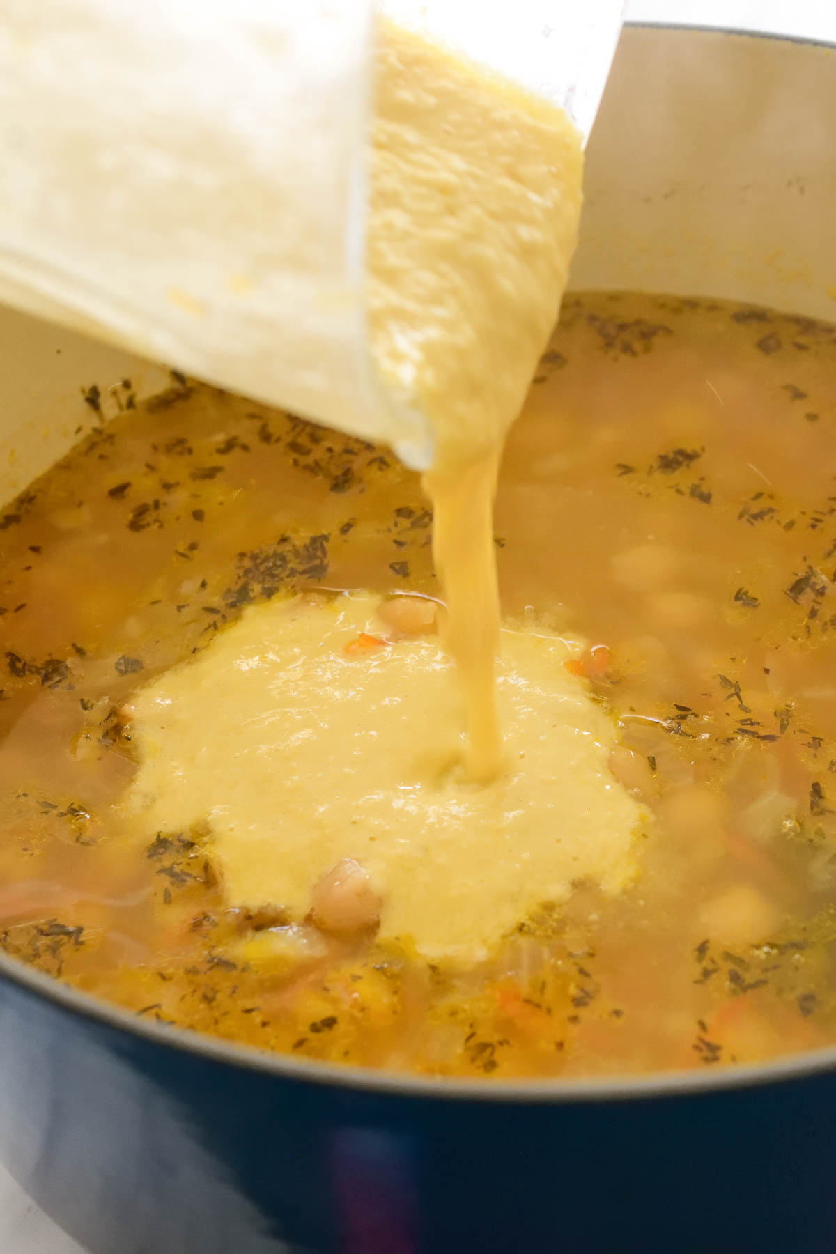 Pouring the blended chickpea mixture into the pot of Greek chickpea soup.