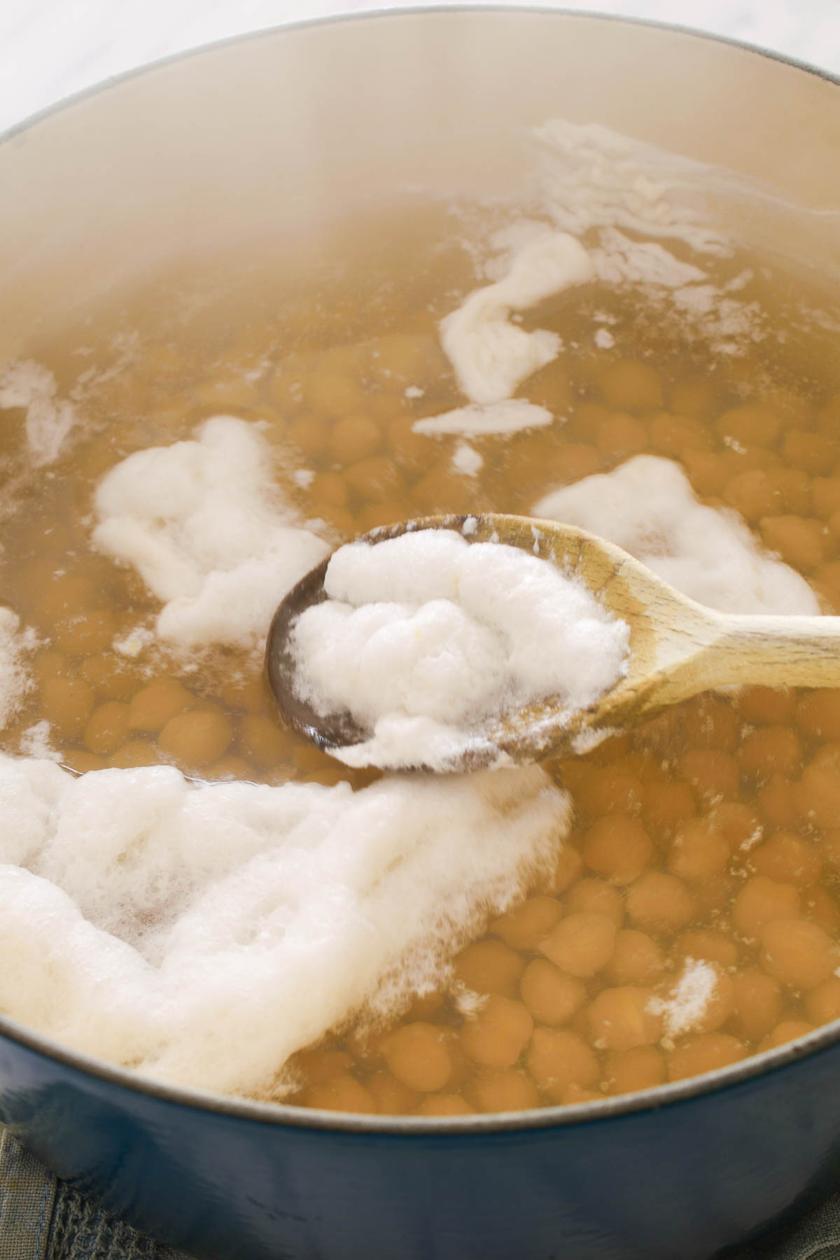 A wooden spoon skimming foam of a pot of boiling chickpeas.
