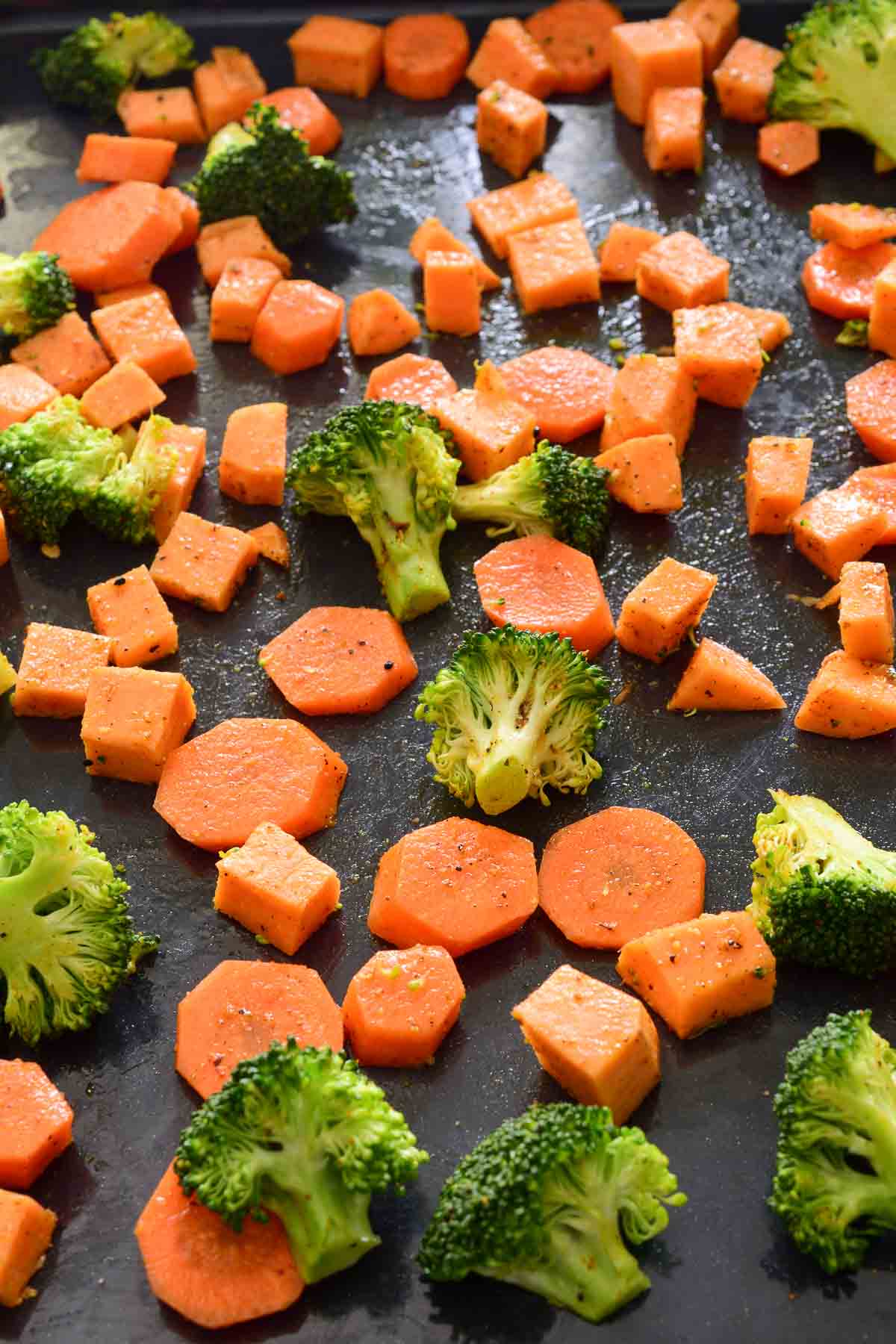 Diced Sweet potato, carrots and broccoli on a black baking pan.