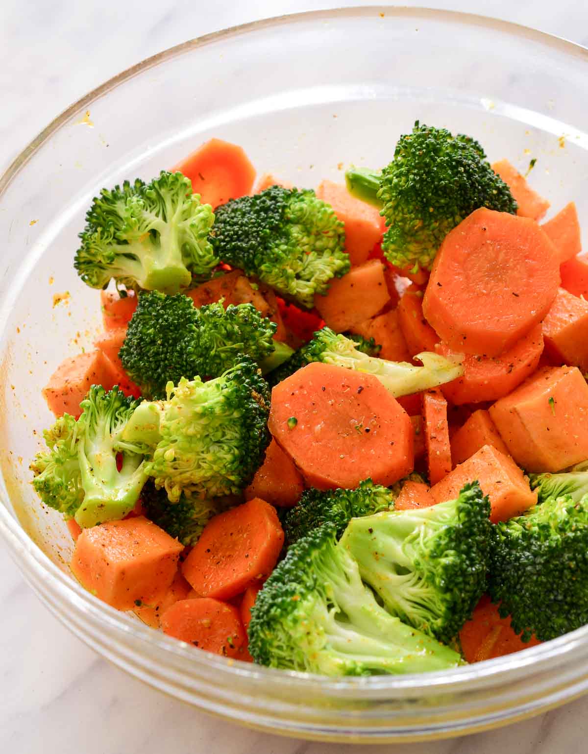 Carrot, sweet potato and broccoli seasoned with ras el hanout in a glass bowl.