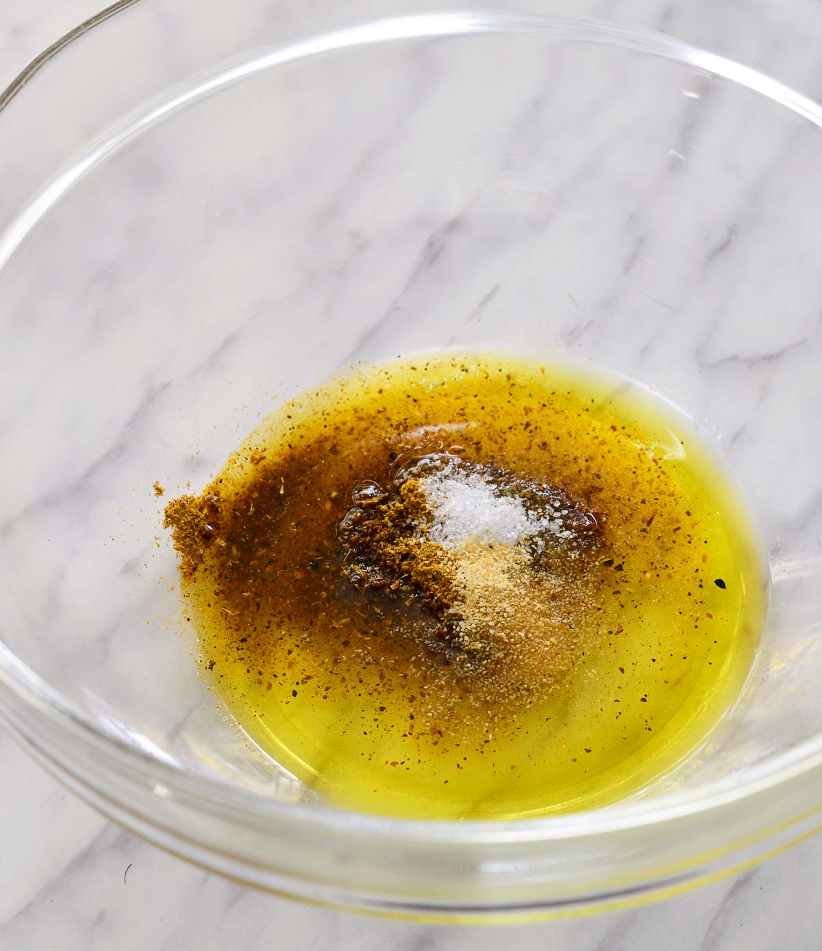 A glass bowl with olive oil, ras el hanout, salt and garlic powder.
