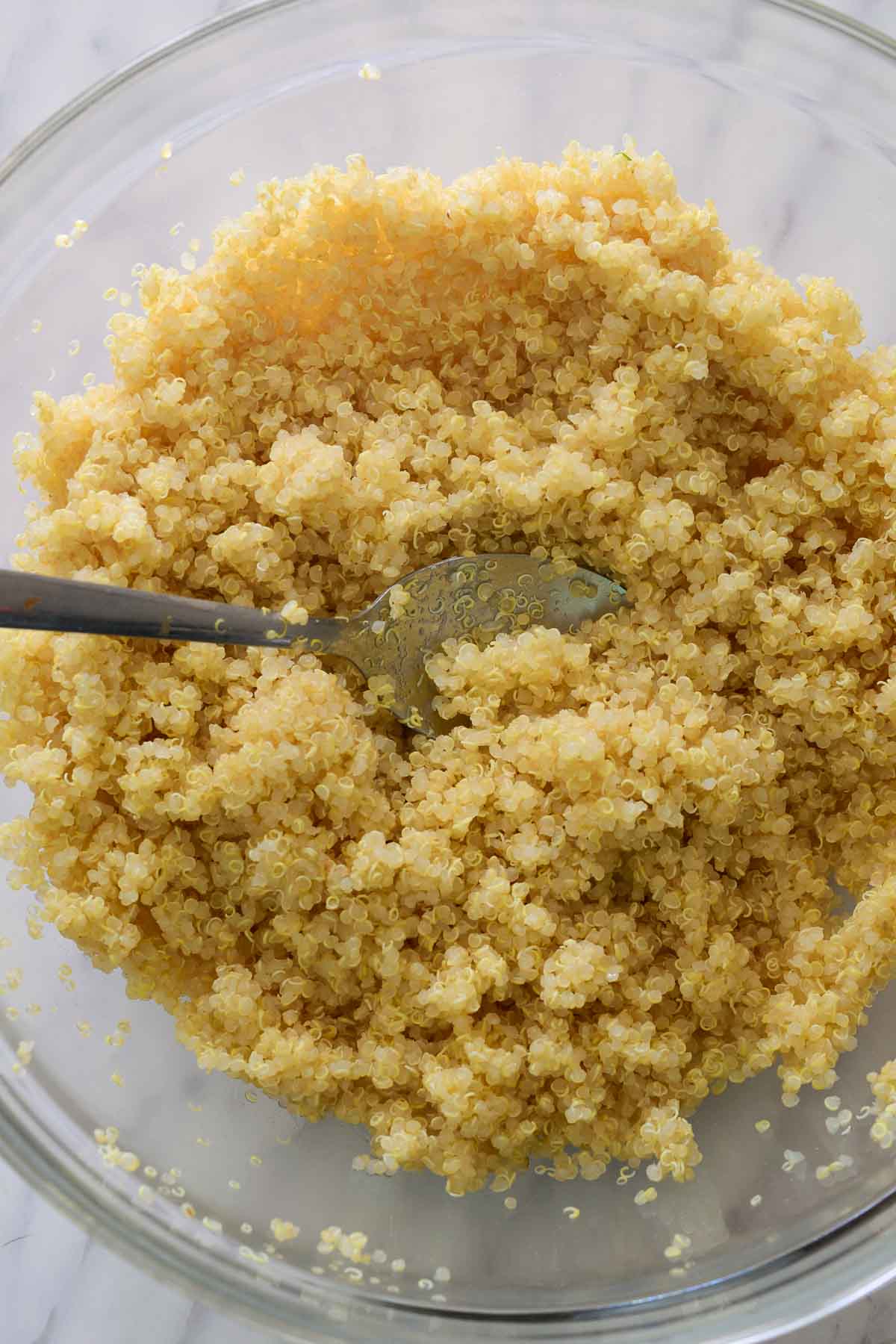 A glass bowl filled with cooked quinoa and a silver spoon.