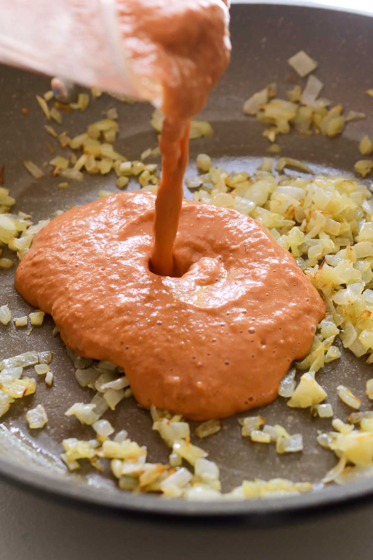 Pouring tomato sauce into a saucepan of fried garlic and onions.