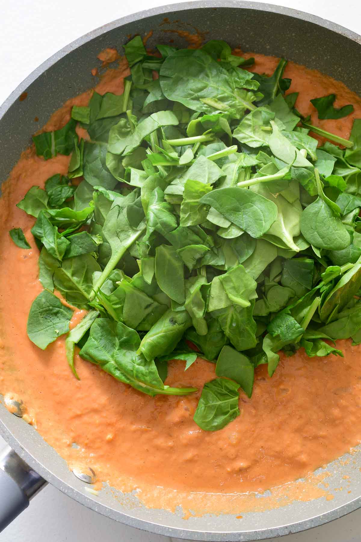 A pile of spinach in the pan of sun dried tomato sauce.