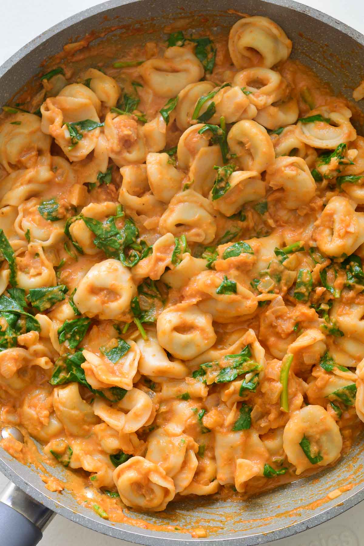 A grey saucepan filled with spinach tortellini in a creamy tomato sauce. 